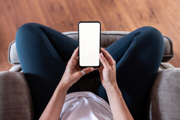 Hands of a girl sitting on an armchair with a smartphone in her hands with the blank screen and crossed legs