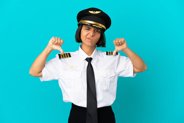 Young airplane pilot over isolated blue background showing thumb down with two hands
