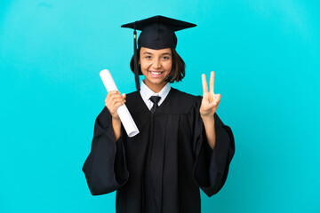 Young university graduate girl over isolated blue background smiling and showing victory sign
