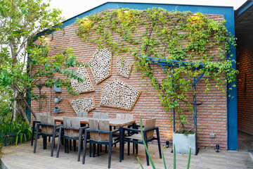 Home decoration designs ,gardening exterior for outdoor dining or party terrace,wine plant hanging on brick wall with many lumber decor on backdrop.Wooden table set on terrace.