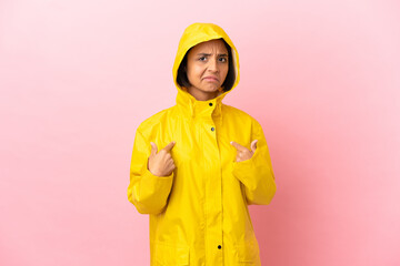 Young latin woman wearing a rainproof coat over isolated background pointing to oneself