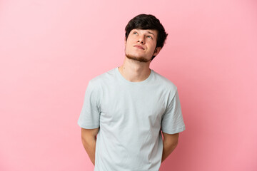 Young Russian man isolated on pink background and looking up