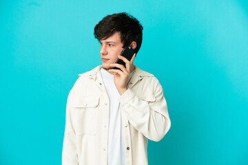 Young Russian man using mobile phone isolated on blue background looking to the side
