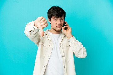 Young Russian man using mobile phone isolated on blue background showing thumb down with negative...