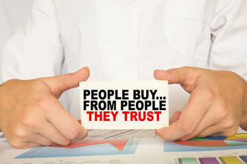 a man in the office holds a card with text PEOPLE BUY... FROM PEOPLE THEY TRUST . business concept