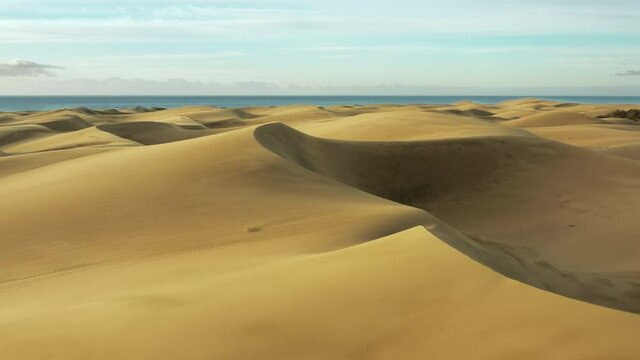 Dunes of golden sand in the hot arid desert. Flying over the sandy desert to the water.