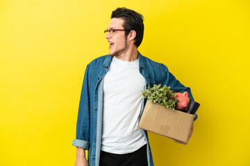 Russian Man making a move while picking up a box full of things isolated on yellow background looking side