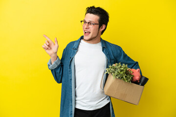 Russian Man making a move while picking up a box full of things isolated on yellow background...