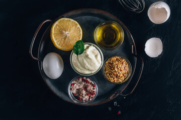 Homemade mayonnaise sauce with ingredient - olive oil, eggs, mustard and lemon on on a metal tray.