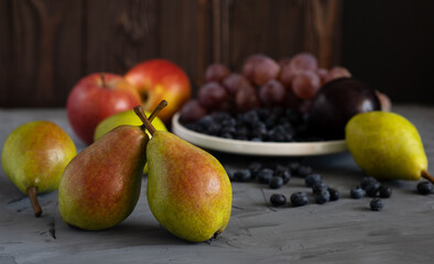 still life of fresh fruits on a gray background, assorted pears, apples, grapes, blueberries close-up