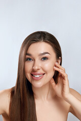 Fototapeta premium Beauty face. Smiling woman touching healthy skin portrait. Beautiful happy girl model with fresh facial skin and natural makeup on grey background. Skin care concept