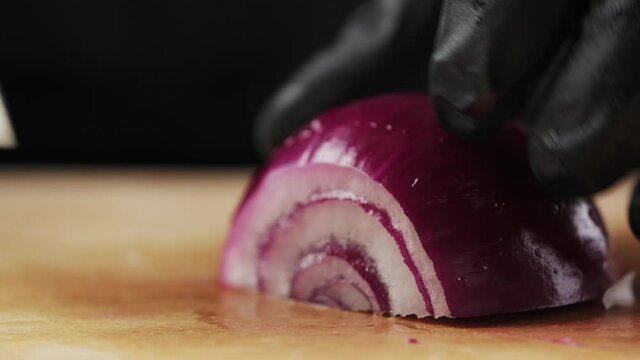 Cutting onions with a knife. Close-up of a chef's hand cuts a red onion with a knife on a wooden board.