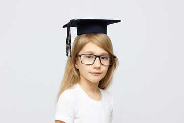 childhood, school, education, learning and people concept - happy girl with glasses in bachelor hat or mortarboard over white background