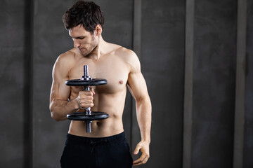 Fototapeta na wymiar Strong handsome man with muscular fit and slim body posing with dumbbell.