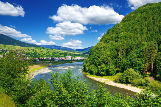 river runs through mountain valley. beautiful summer countryside landscape. village in the distance. wonderful scenery view. fluffy clouds on the deep blue sky