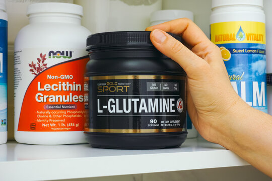 Tambov, Russian Federation - January 25, 2021 Woman hand taking jar of L-Glutamine by California Gold Nutrition out of kitchen cupboard