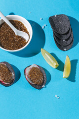Superfood, vegetarian snack, lean dish. Black potato chips with chia seed caviar on a blue background.Vertical frame, Close-up, hard shadows.