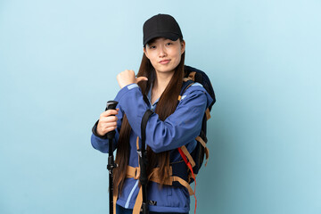 Young Chinese girl with backpack and trekking poles over isolated blue background proud and self-satisfied
