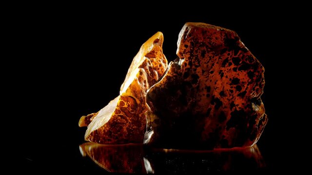 Large parts of broken natural yellow amber stone rotate under bright electric light macro. Concept precious gemstone