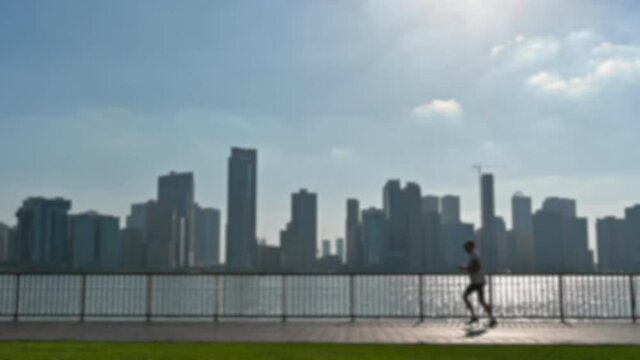Slow-motion, Out of focus: A Young man exercising with outdoor running with a city view in the background at Khalid Lake in Sharjah, United Arab Emirates