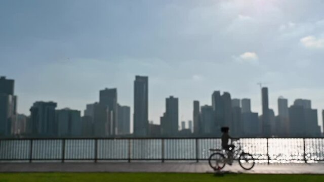 Slow-motion, Out of focus: A girl riding a bike, having fun outdoors with a city view in the background at Khalid Lake in Sharjah, United Arab Emirates