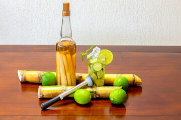 More traditional Brazilian caipirinha on the wooden table with lemon, cachaça with pieces of sugar cane, sugar cane and lemon kneader