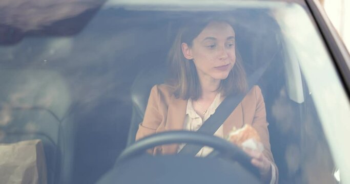 Business Woman Eats A Burger On The Go While Driving A Car