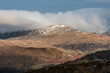 Majestic Winter landscape image view from Holme Fell in Lake District towards snow capped mountain ranges in distance in glorious evening light with Autumnal colors trees