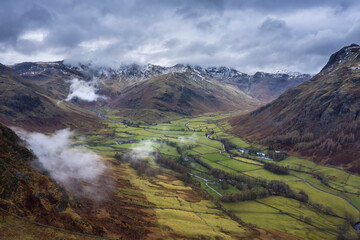 Stunning flying drone landscape image of Langdale pikes and valley in Winter with dramatic low level clouds and mist swirling around