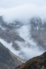 Epic Winter landscape image of view from Side Pike towards Langdale pikes with low level clouds on mountain tops and moody mist swirling around