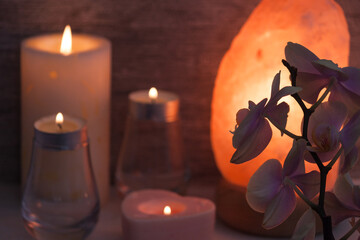 Himalayan salt lamp with orchid flower, candles, blurry in dark room. Spa, relax concept. - obrazy, fototapety, plakaty