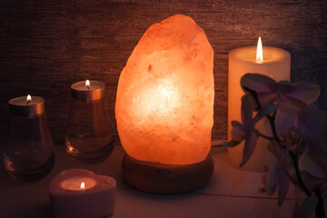 Himalayan salt lamp with orchid flower, candles in dark room. Spa, relax concept.
