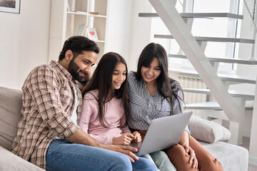 Happy indian family couple with child daughter using laptop computer at home. Smiling parents and teen kid bonding watching streaming online tv or doing ecommerce shopping together sitting on sofa.