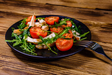 Roasted chicken breasts and salad with arugula and cherry tomatoes in a black plate