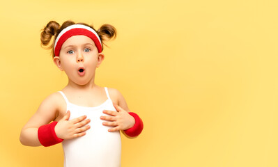Excited fitness child posing in sportswear,red wristbands,headband over yellow studio background. Children sport,advertising,shopping concept.Gym workout.Childhood activity.Sport.Health and energy
