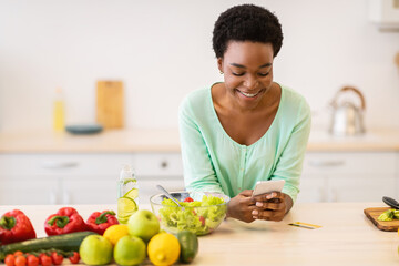 Happy African Lady Using Smartphone With Cooking Application In Kitchen