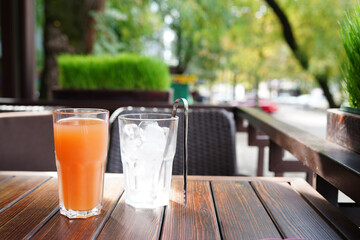 Orange juice with ice on wooden table in the cafe outdoors, summer drinks