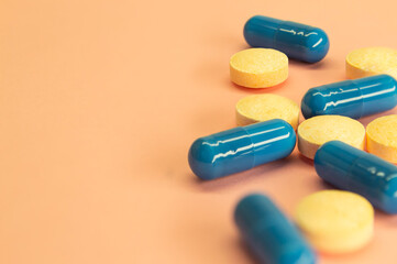 Orange pills and blue capsules on a peach background with space for text. Medicine image. Healthcare. 