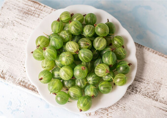 Fresh green gooseberries in a white plate on a wooden background. summer vitamin harvest. The view from top