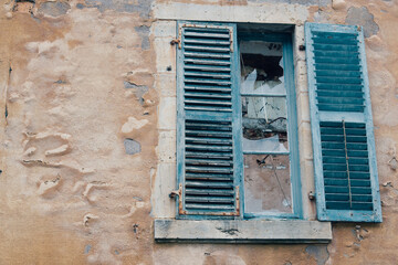 une fenêtre cassée sur un mur détérioré. Une fenêtre abandonnée. Une fenêtre bleue sur un mur orange.