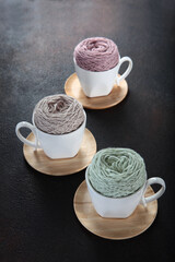 Colorful balls of yarn in white ceramic cups. White cups on wooden saucers. The concept of hand...