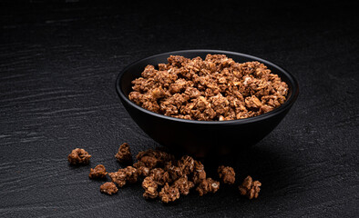Chocolate granola on black background, bowl of crunchy muesli