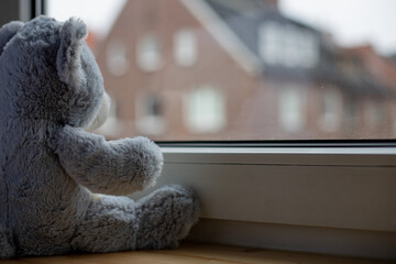 Stuffed animal looking out of a window, symbolizing isolated children during lockdown or quarantine during the corona pandemic