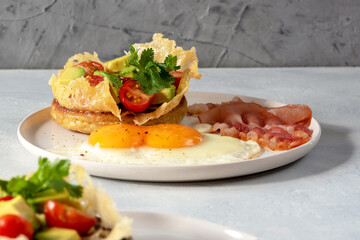 Crumpets are traditional in English-speaking countries lush pancakes made from yeast dough with cheese, avocado and cherry tomatoes. With eggs and fried bacon for breakfast. Selective focus.