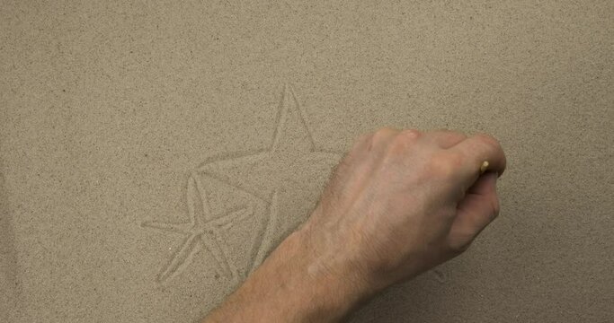 Artist paints in the sand in real time. Stars, seashell and flip flops stick out of the sand against the backdrop of the sunset. Concept for holiday, travel and vacation background