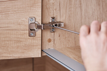 Hand screwing door hinge on kitchen cabinet - obrazy, fototapety, plakaty