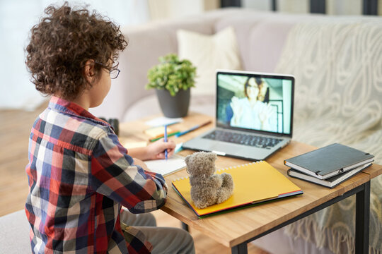 Get The Knowledge. Rear View Of Hispanic School Boy Making Notes During Online Lesson With Teacher Via Video Chat App. Child Using Laptop While Studying At Home