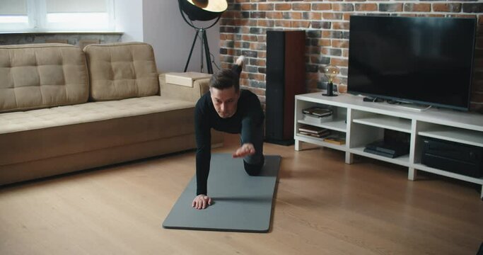 Training At Home. Sporty man doing yoga plank while watching online tutorial on mobile, exercising in living room, free space. High quality 4k footage