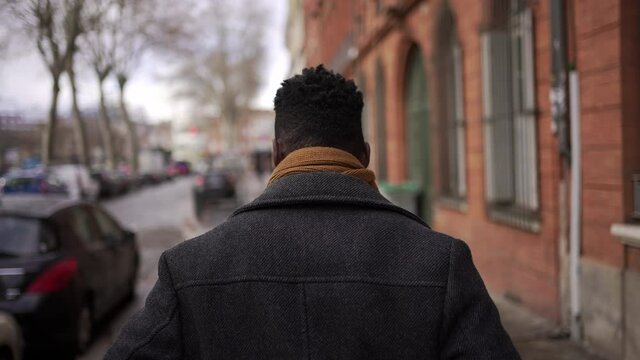 Black Man Walking Outdoors In City Sidewalk During Winter. Back Of African Person In Downtown