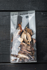 Dried mushrooms, on black wooden table background, in plastic pack, top view flat lay